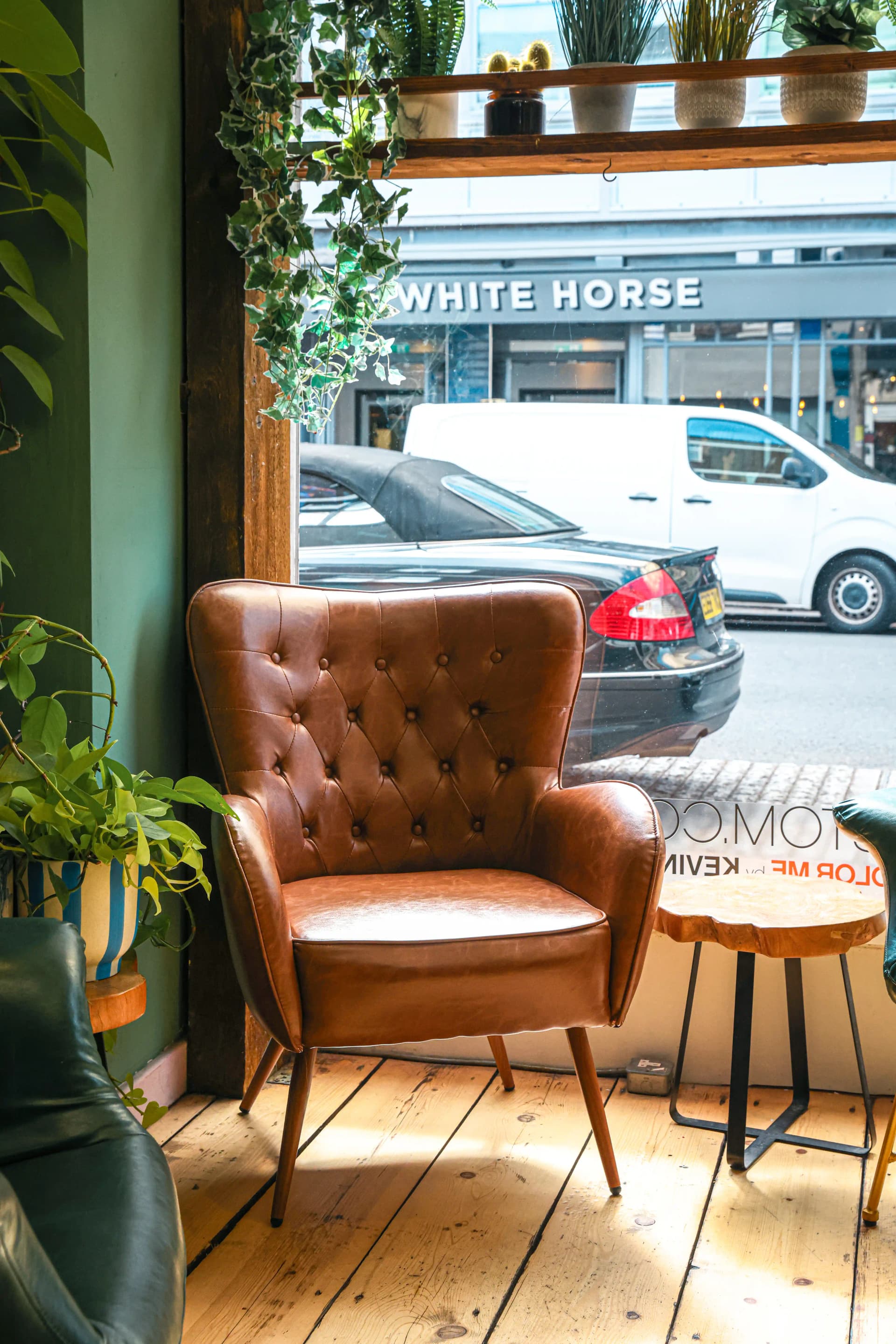The welcoming seating area at Fern & Flow Hair salon in Beckenham — tan leather armchair, natural light, and hanging ivy